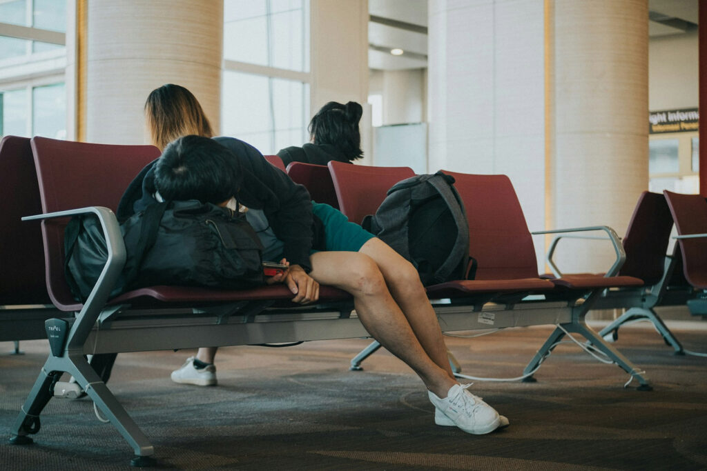 Traveler slumped on an airport bench, demonstrating poor posture that can worsen back pain during holiday travel.