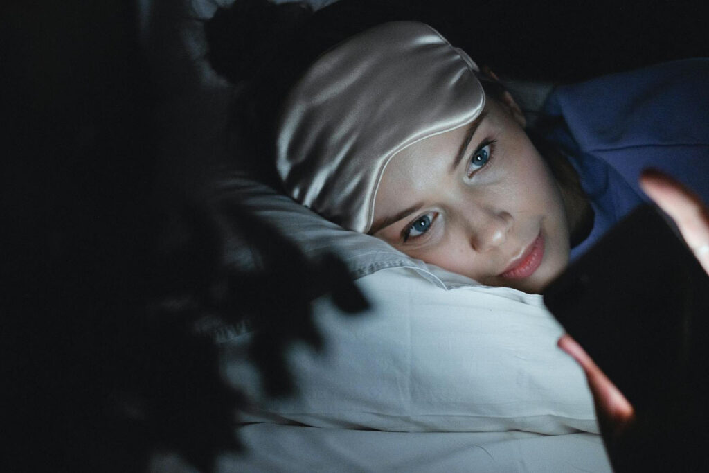 Person lying in bed at night using a phone, showing how screen use makes it harder to sleep better naturally